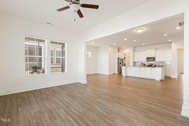 unfurnished living room with light wood finished floors, baseboards, and visible vents