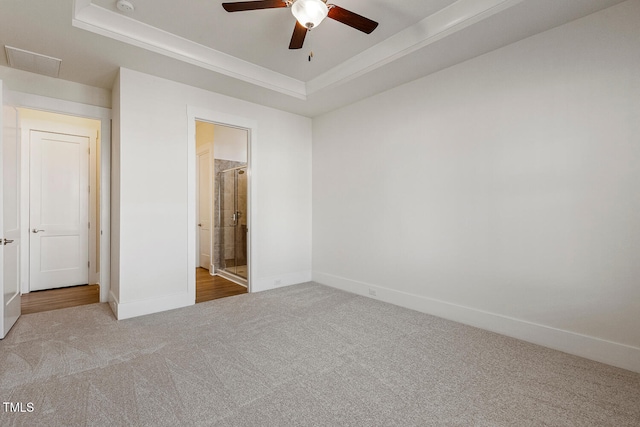 unfurnished bedroom featuring carpet floors, a tray ceiling, visible vents, a ceiling fan, and baseboards