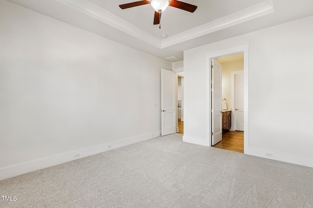 unfurnished bedroom with a raised ceiling, a ceiling fan, carpet flooring, connected bathroom, and baseboards