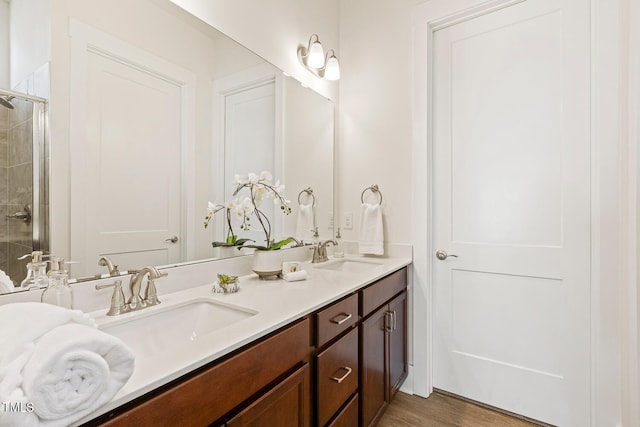 bathroom featuring wood finished floors, a sink, a shower stall, and double vanity