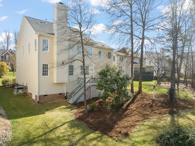 rear view of house with a chimney, a lawn, central AC unit, crawl space, and stairs