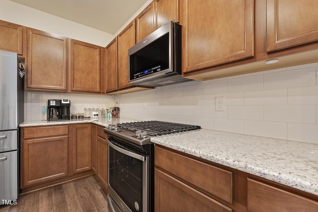 kitchen with dark wood-style floors, appliances with stainless steel finishes, backsplash, and brown cabinets