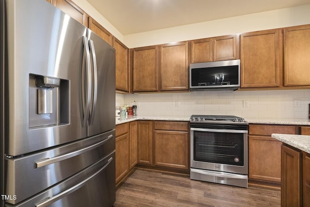 kitchen with appliances with stainless steel finishes, dark wood-style flooring, brown cabinetry, and tasteful backsplash