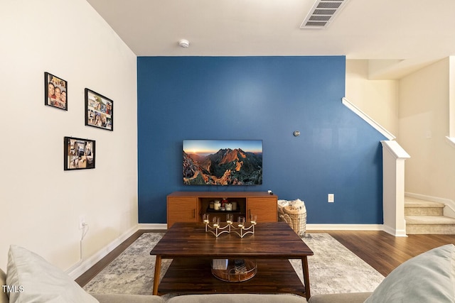 living room with stairs, visible vents, baseboards, and wood finished floors