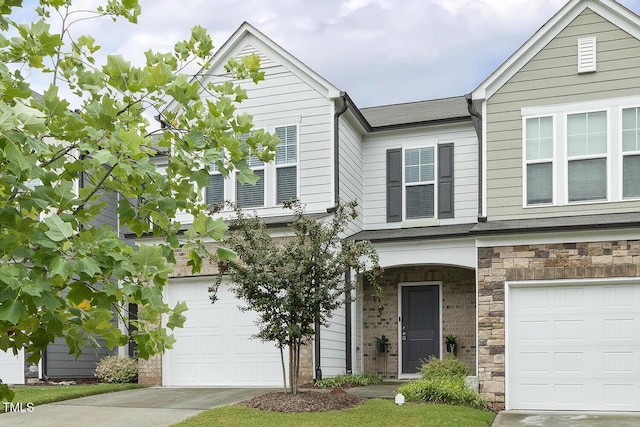 townhome / multi-family property featuring a garage, stone siding, and concrete driveway