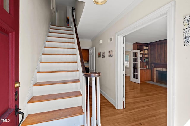 stairway with a brick fireplace, crown molding, baseboards, and wood finished floors