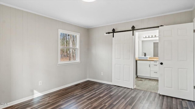 unfurnished bedroom featuring crown molding, dark wood finished floors, a sink, and a barn door