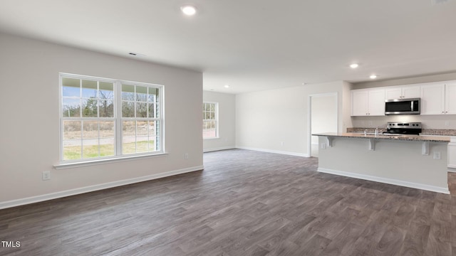 kitchen featuring white cabinetry, light stone counters, dark wood-type flooring, appliances with stainless steel finishes, and a kitchen bar