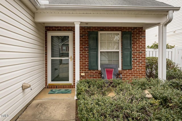 entrance to property with a shingled roof and brick siding