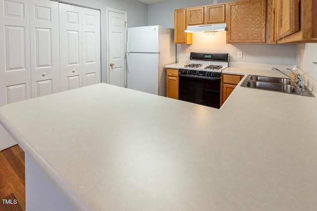 kitchen with freestanding refrigerator, gas range oven, light countertops, under cabinet range hood, and a sink