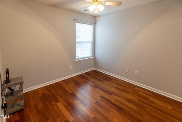 empty room featuring a textured ceiling, visible vents, a ceiling fan, baseboards, and dark wood finished floors