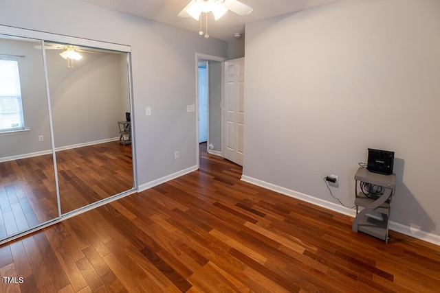 unfurnished bedroom featuring a ceiling fan, baseboards, dark wood finished floors, and a closet