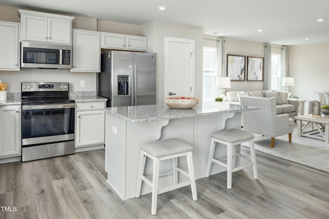 kitchen with white cabinetry, a kitchen island, stainless steel appliances, and light stone counters