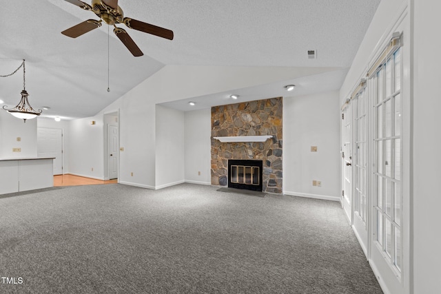 unfurnished living room featuring baseboards, carpet, vaulted ceiling, a textured ceiling, and a stone fireplace