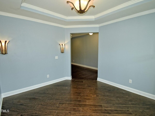 spare room featuring dark wood-style floors, a tray ceiling, crown molding, and baseboards