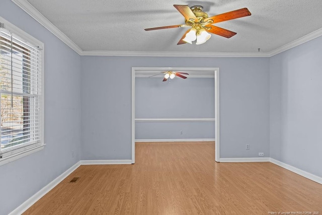 unfurnished room with a textured ceiling, wood finished floors, visible vents, baseboards, and crown molding