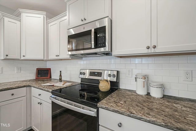 kitchen featuring dark stone counters, stainless steel appliances, decorative backsplash, and white cabinets