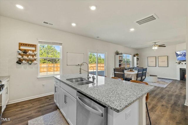 kitchen featuring a center island with sink, light stone counters, stainless steel dishwasher, sink, and white cabinetry