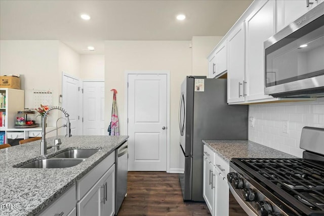 kitchen featuring stainless steel appliances, light stone countertops, backsplash, sink, and white cabinetry