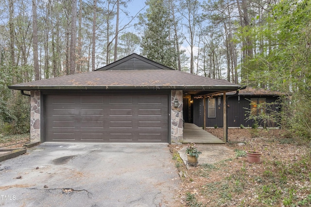 view of front facade featuring stone siding, driveway, a garage, and roof with shingles