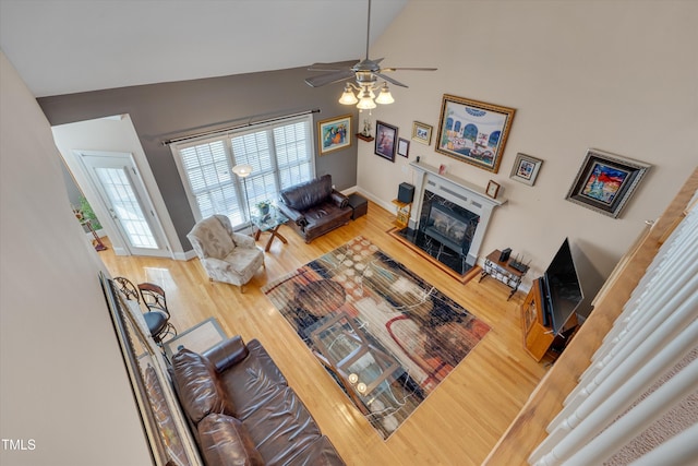 living area featuring baseboards, a ceiling fan, a glass covered fireplace, wood finished floors, and high vaulted ceiling