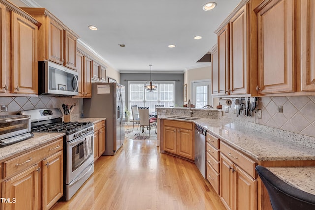 kitchen featuring light stone counters, decorative light fixtures, stainless steel appliances, crown molding, and a sink