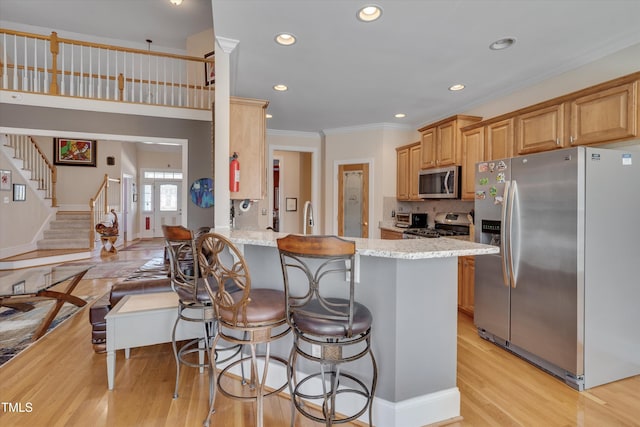 kitchen featuring light wood-style flooring, appliances with stainless steel finishes, light stone counters, a peninsula, and crown molding