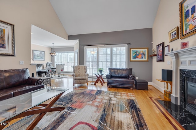 living room featuring light wood-style floors, baseboards, a premium fireplace, and high vaulted ceiling