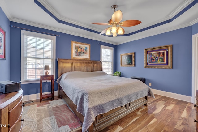 bedroom with ornamental molding, a raised ceiling, baseboards, and wood finished floors