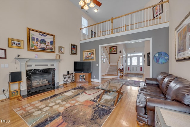 living area featuring baseboards, a towering ceiling, a premium fireplace, stairway, and wood finished floors