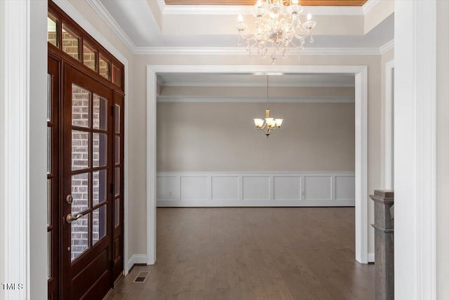 entryway featuring dark wood-style floors, ornamental molding, an inviting chandelier, a tray ceiling, and a decorative wall