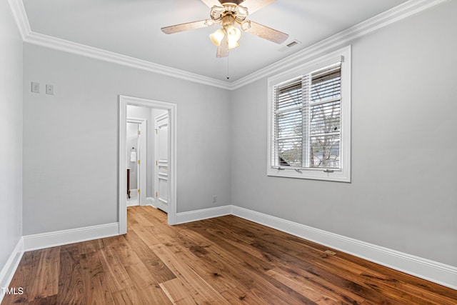 empty room featuring visible vents, ornamental molding, wood finished floors, baseboards, and ceiling fan