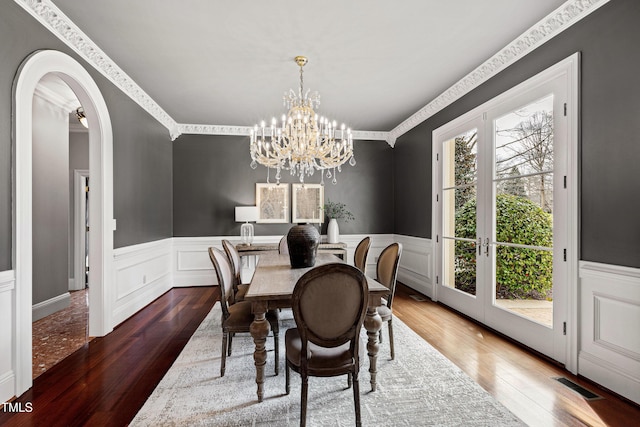 dining area with arched walkways, visible vents, a wainscoted wall, and wood finished floors