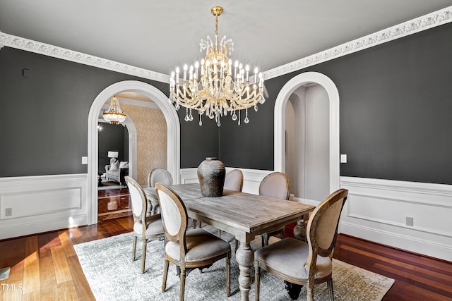 dining area featuring arched walkways, wood finished floors, and wainscoting