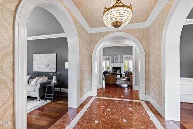 hallway featuring wallpapered walls, a notable chandelier, arched walkways, and baseboards