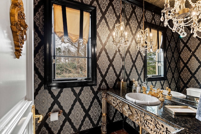 bathroom with a sink, a notable chandelier, and wallpapered walls