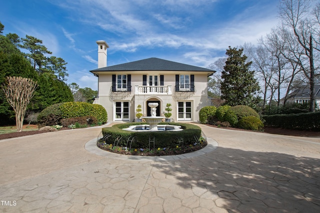 view of front of home with curved driveway, a chimney, a balcony, and stucco siding