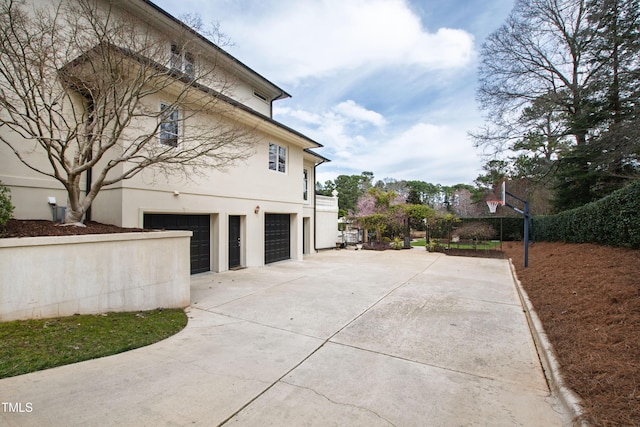 view of side of home featuring concrete driveway, an attached garage, and stucco siding