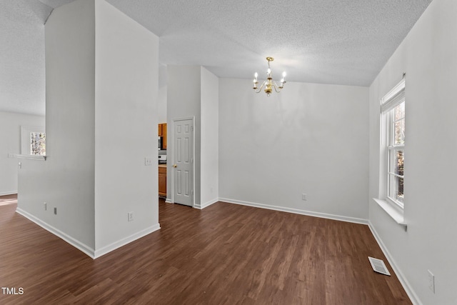 empty room featuring dark wood-type flooring, a wealth of natural light, and a notable chandelier