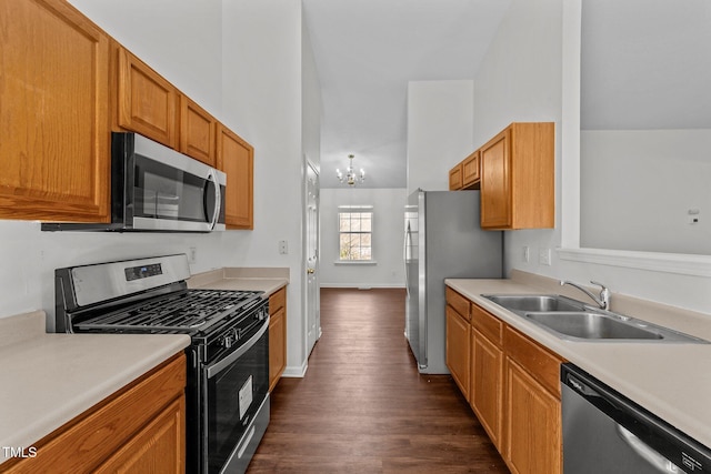 kitchen with appliances with stainless steel finishes, light countertops, a sink, and dark wood-type flooring