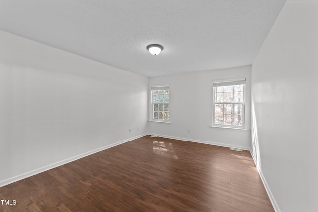 empty room featuring dark wood-style floors, a textured ceiling, and baseboards