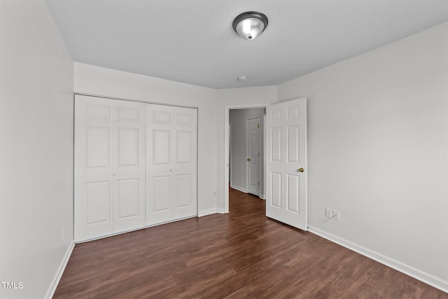 unfurnished bedroom with a textured ceiling, a closet, dark wood finished floors, and baseboards