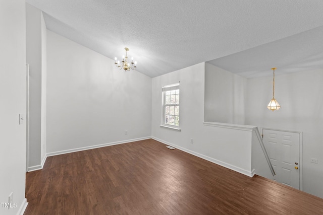 spare room featuring a notable chandelier, lofted ceiling, a textured ceiling, wood finished floors, and baseboards