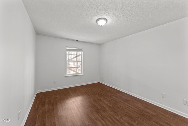 empty room with a textured ceiling, dark wood-style flooring, and baseboards