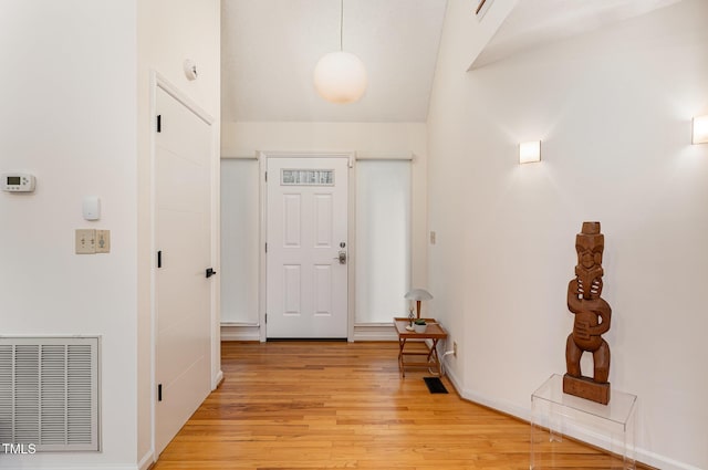 hall featuring lofted ceiling, light wood-style flooring, and visible vents