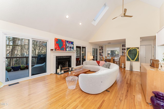 living area featuring high vaulted ceiling, light wood-style flooring, a skylight, a fireplace, and visible vents