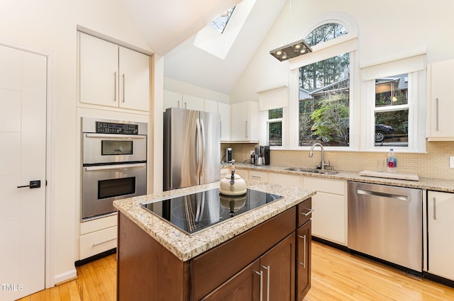 kitchen featuring stainless steel appliances, light wood-style floors, lofted ceiling with skylight, white cabinets, and a sink