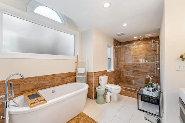 bathroom featuring visible vents, toilet, a soaking tub, a shower stall, and tile walls