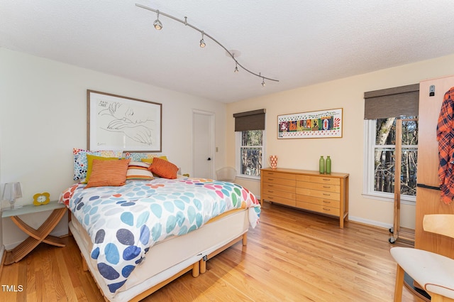 bedroom featuring light wood-style floors, track lighting, baseboards, and a textured ceiling