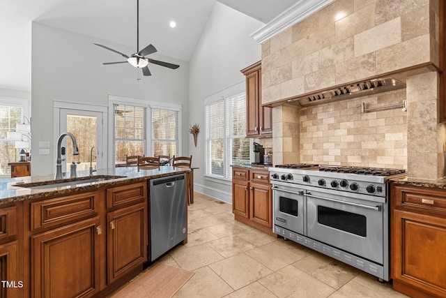 kitchen featuring a sink, appliances with stainless steel finishes, brown cabinets, dark stone counters, and custom range hood